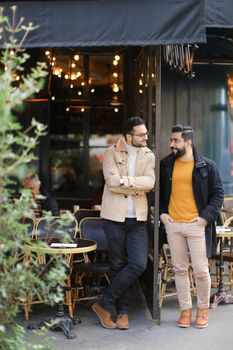 Two fashionable caucasian men standing and talking at street cafe. Concept of friendship and friends meeting.