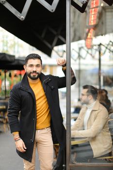 Young fashionable man standing at street cafe outdoors. Concept of life style and male fashion.