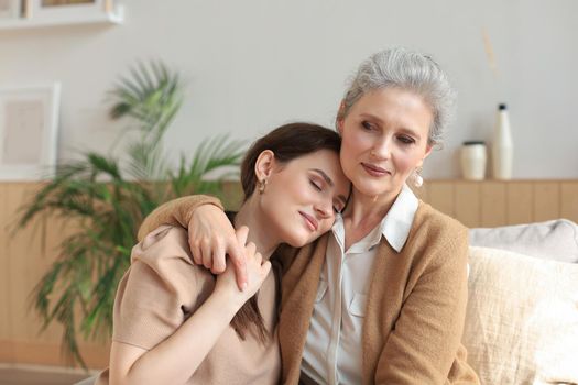 Portrait of old mother and mature daughter hugging at home. Happy senior mom and adult daughter embracing with love on sofa
