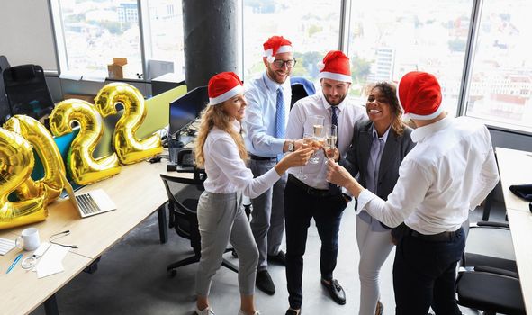 Business people are celebrating holiday in modern office drinking champagne and having fun in coworking. Merry Christmas and Happy New Year 2022