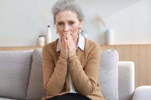 Worried middle aged woman sitting on a sofa in the living room