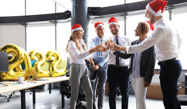 Business people are celebrating holiday in modern office drinking champagne and having fun in coworking. Merry Christmas and Happy New Year 2022