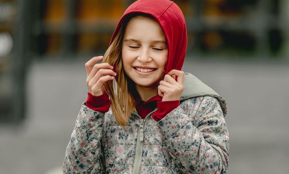 Preteen girl wearing hood and smiling at the street at autumn. Pretty female kid fall portrait outdoors