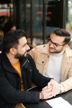 Two young cacuasian gays talking at street cafe and holding hands. Concept of same sex couple and lgbt.
