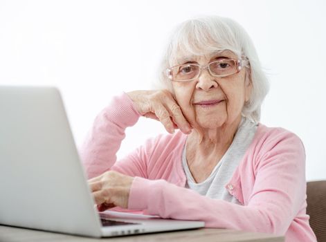 Senior woman with laptop sitting at home and looking at the camera. Portrait of elderly person with modern technologies