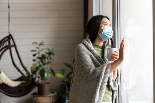 Asian girl in medical face mask, yearning go outside, being sick with covid 19 and staying on self quarantine in her house.