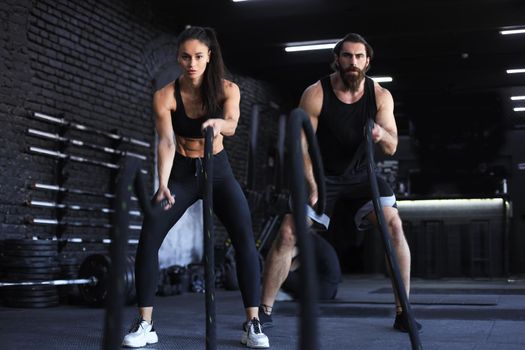 Athletic young couple with battle rope doing exercise in functional training fitness gym