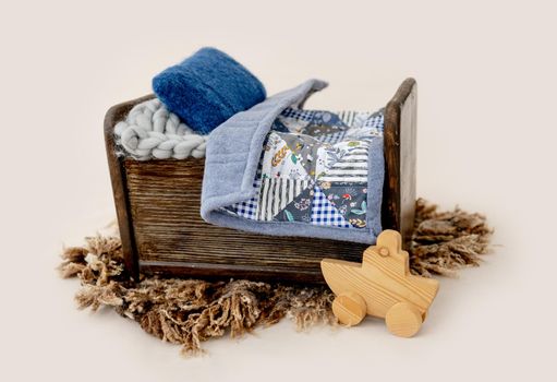 Decoration for newborn studio photoshoot. Tiny bed with handmade blanket and wooden toy for infant baby photos