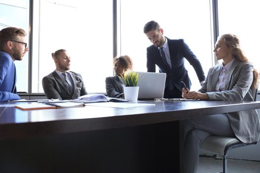 Group of modern business people in formalwear discussing business and smiling while sitting in the office.