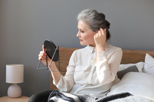 mature woman looking at mirror and touching face at home
