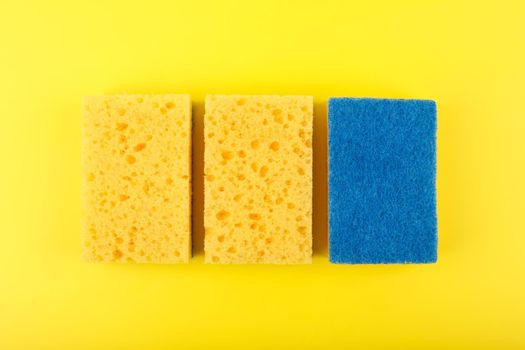 Flat lay with three yellow cleaning and dishwashing sponges on yellow background. Close up, dishwashing or house cleaning concept