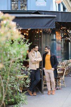 Two cheerful caucasian men standing and talking at street cafe. Concept of friendship and friends meeting.