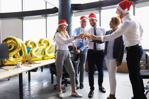 Business people are celebrating holiday in modern office drinking champagne and having fun in coworking. Merry Christmas and Happy New Year 2022