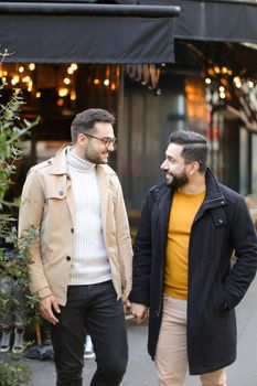 Two young caucasian gays standing at street cafe and holding hands. Concept of same sex couple and male friendship.