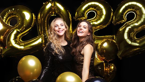 Happy gorgeous girls in stylish sexy party dresses holding gold 2022 balloons, having fun at Christmas or New Year's Eve Party