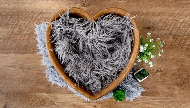 Decoration for newborn studio photoshoot. Tiny wooden shape heart bed with fur and flowers for infant baby photos