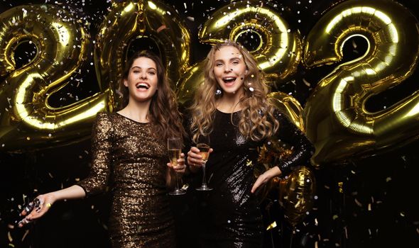 Two young ladies drinking champagne. Image of girls with balloons isolated on black background, having fun at Christmas or New Year's 2022 Eve Party