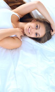 A beautiful young woman lying in bed comfortably and blissfully.