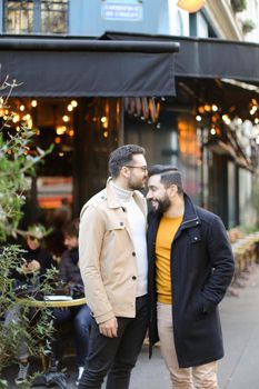 Two young gays standing at street cafe and smiling. Concept of same sex couple and male friendship.
