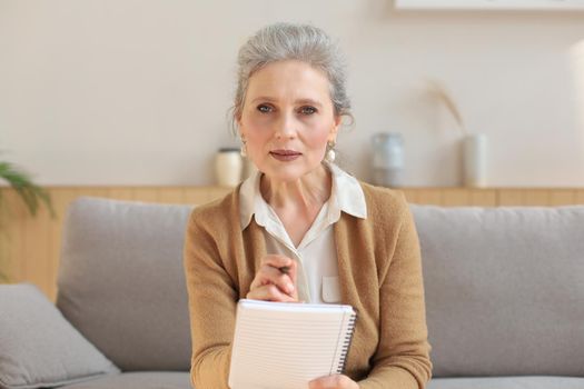 Attractive mature woman sitting on the couch and making notes in diary
