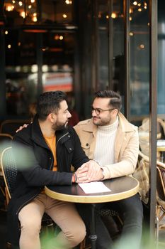 Two european gays talking at street cafe and holding hands. Concept of same sex couple and lgbt.
