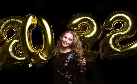 Happy gorgeous girl in stylish sexy party dress holding gold 2022 balloons, having fun at Christmas or New Year's Eve Party