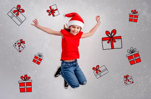 Little girl in santa hat jumping between christmas presents drawings painted on white wall