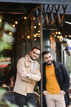 Two young gays standing at street cafe and smiling. Concept of same sex couple and male friendship.