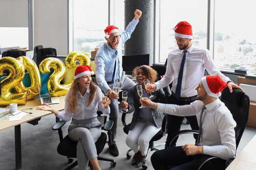 Business people are celebrating holiday in modern office drinking champagne and having fun in coworking. Merry Christmas and Happy New Year 2022