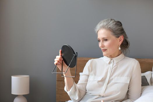 mature woman looking at mirror and touching face at home