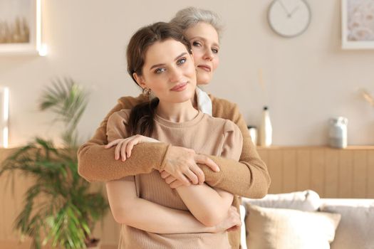 Beautiful mother and daughter. Cheerful young woman is embracing her middle aged mother in living room. Family portrait