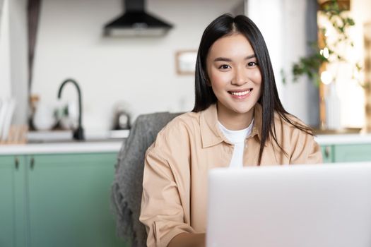 Smiling asian woman working from home with laptop. Happy girl using computer to study or work, freelance and remote education concept.