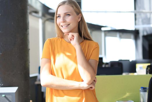 Attractive business woman in smart casual wear looking at camera and smiling while standing in the office.