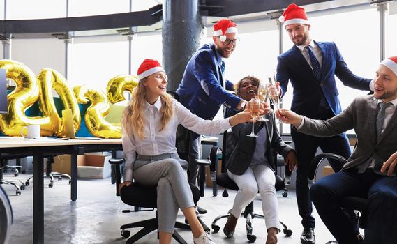 Business people are celebrating holiday in modern office drinking champagne and having fun in coworking. Merry Christmas and Happy New Year 2022
