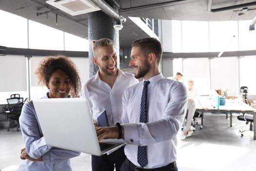 Group of modern business people are working using laptop and smiling while standing in the office hallway.