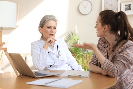 Middle aged female doctor therapist in consultation with patient in office