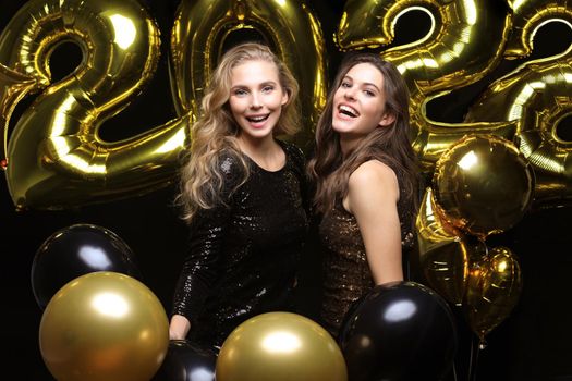 Happy gorgeous girls in stylish sexy party dresses holding gold 2022 balloons, having fun at Christmas or New Year's Eve Party