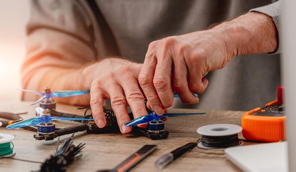 Closeup view of service man hands screw blue propeller of quadcopter