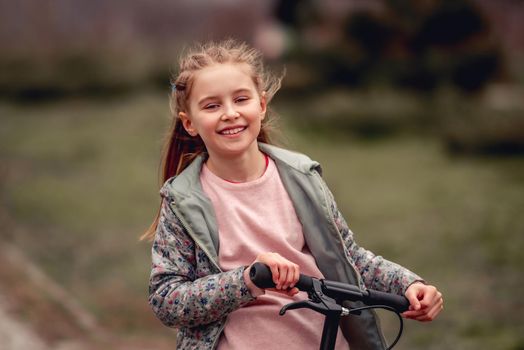 Closeup portrait of beautiful little girl riding on scooter in the park