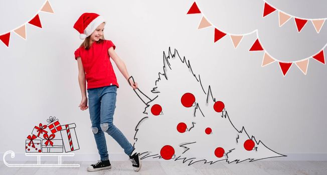 Little girl carrying sketch of decorated christmas tree on white wall background