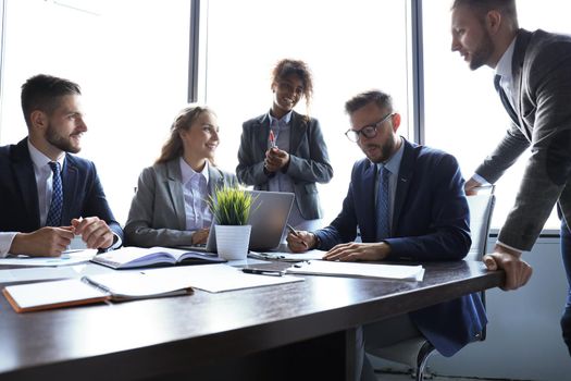 Group of modern business people in formalwear discussing business and smiling while sitting in the office.