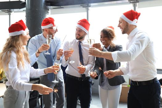 Young business partners are lighting bengal lights and drinking champagne in a modern office. Merry Christmas and Happy New Year