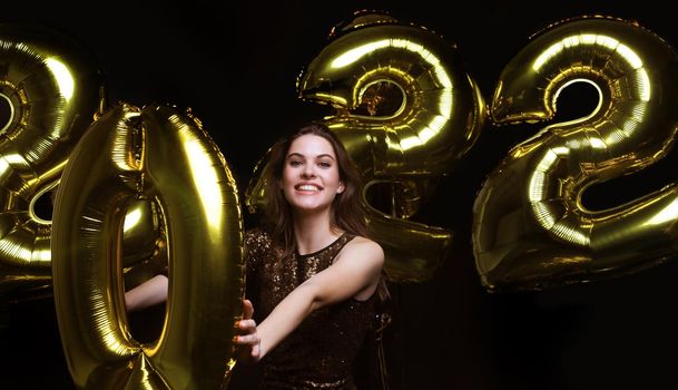 Happy gorgeous girl in stylish sexy party dress holding gold 2022 balloons, having fun at Christmas or New Year's Eve Party