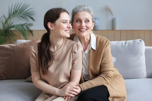 Portrait of old mother and mature daughter hugging at home. Happy senior mom and adult daughter embracing with love on sofa