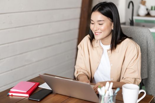 Smiling asian woman tutor, teacher teaching lesson at online language school, using laptop to work remotely, e-learning and distance education concept.