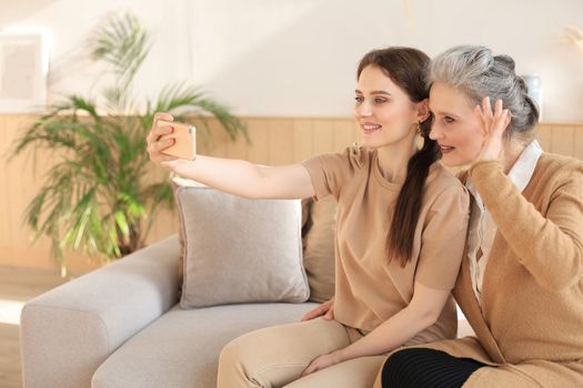 Happy middle aged mother and daughter taking selfie at home