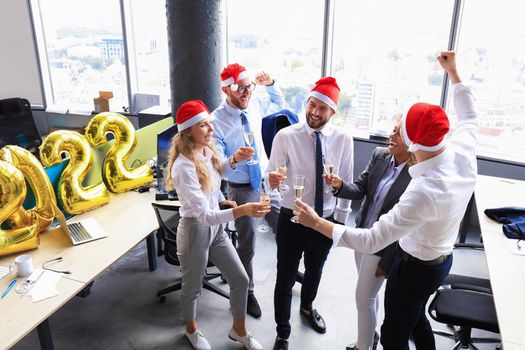 Business people are celebrating holiday in modern office drinking champagne and having fun in coworking. Merry Christmas and Happy New Year 2022