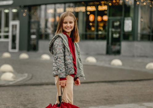 Preteen girl with umbrella in rainy evening at autumn looking at camera and smiling. Pretty kid portrait outdoors