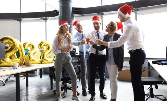 Business people are celebrating holiday in modern office drinking champagne and having fun in coworking. Merry Christmas and Happy New Year 2022