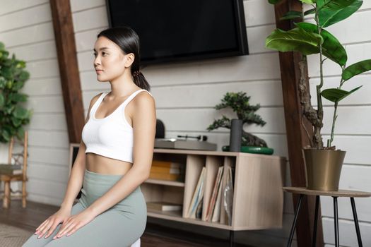 Image of asian woman getting concentrated during morning meditation, practice yoga at home, sitting in living room, zen pose.
